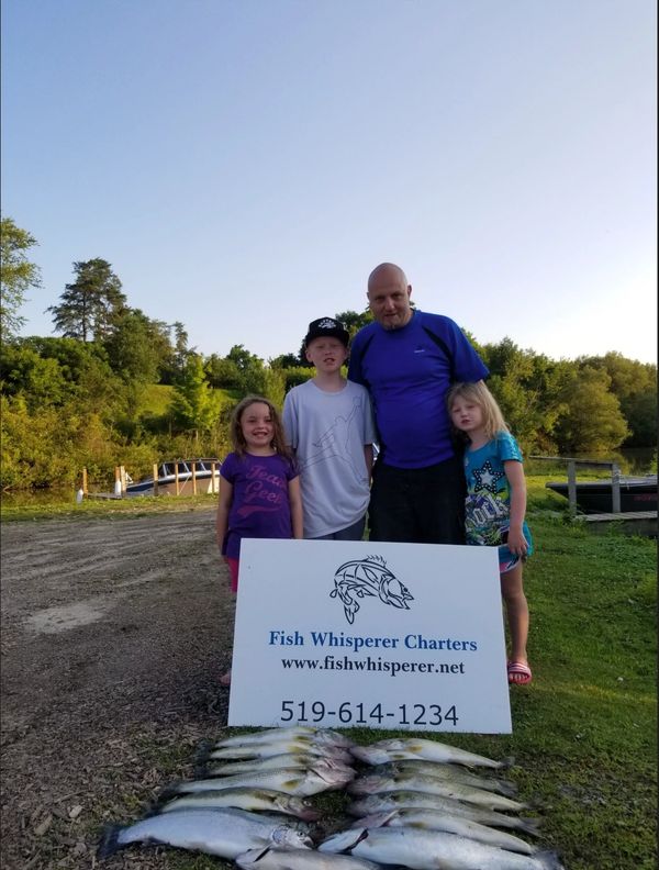 Family with caught fish and Fish Whisperer Charters sign outdoors.