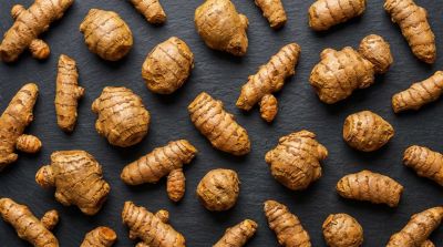 Fresh turmeric roots arranged on a dark surface.