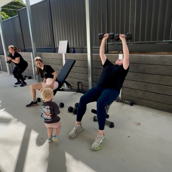Three women exercising outdoors with a child watching.