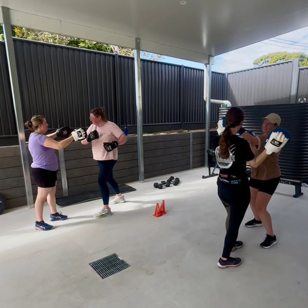 Two pairs of women boxing in a covered outdoor space.