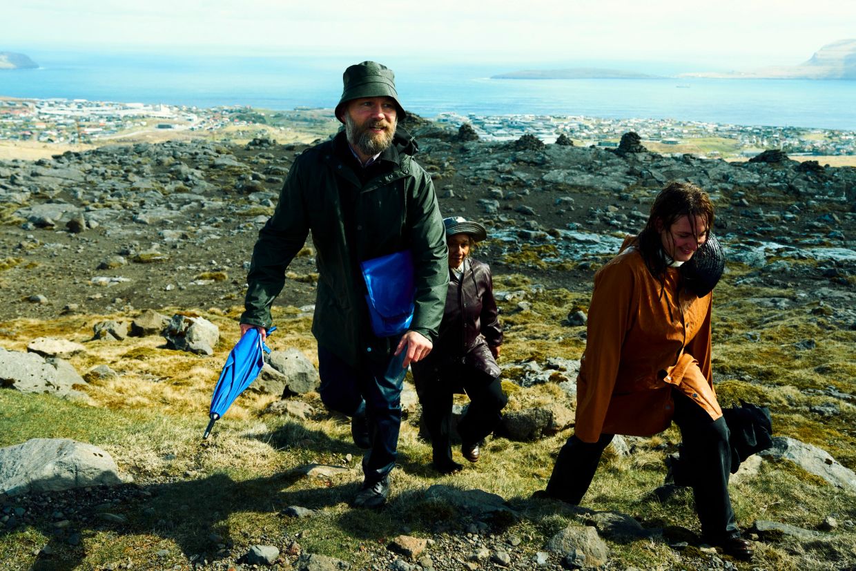 Three people hiking uphill on a rocky landscape overlooking a coastal town.