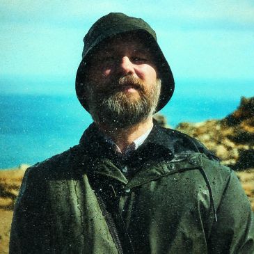 Man with a beard wearing a rain jacket and bucket hat outdoors.