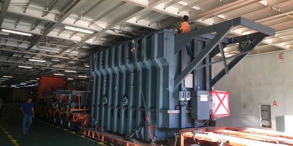 Large industrial transformer being transported indoors on a heavy-duty trailer.