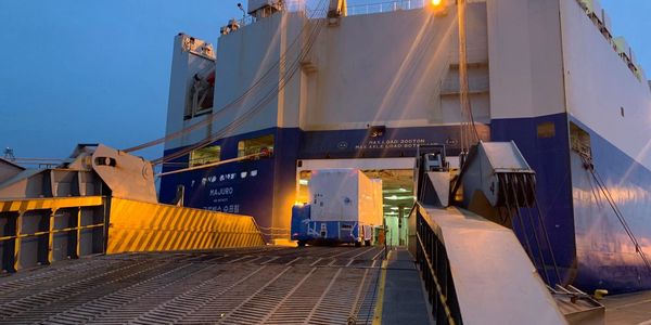 Cargo vehicle boarding a large ship at dusk.