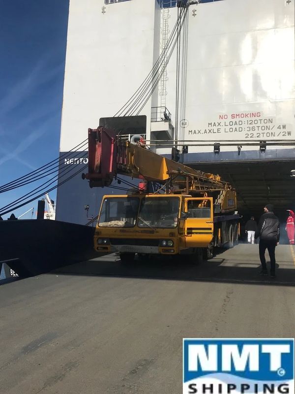 Yellow crane truck unloading from a large cargo ship under clear blue sky.