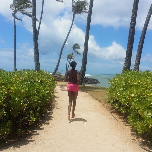 Woman walking on a sandy path by the beach with palm trees.