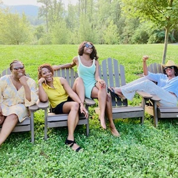 Four women relaxing outdoors on wooden chairs.