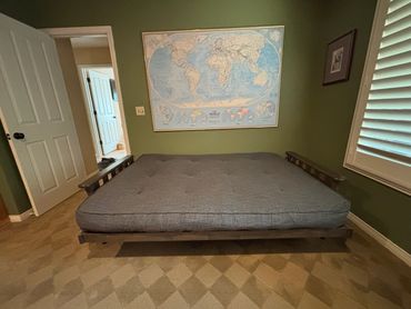 A gray futon bed in a green-walled room with a world map on the wall.