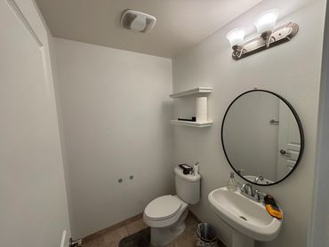 Minimalist bathroom with toilet, sink, round mirror, and wall shelves.