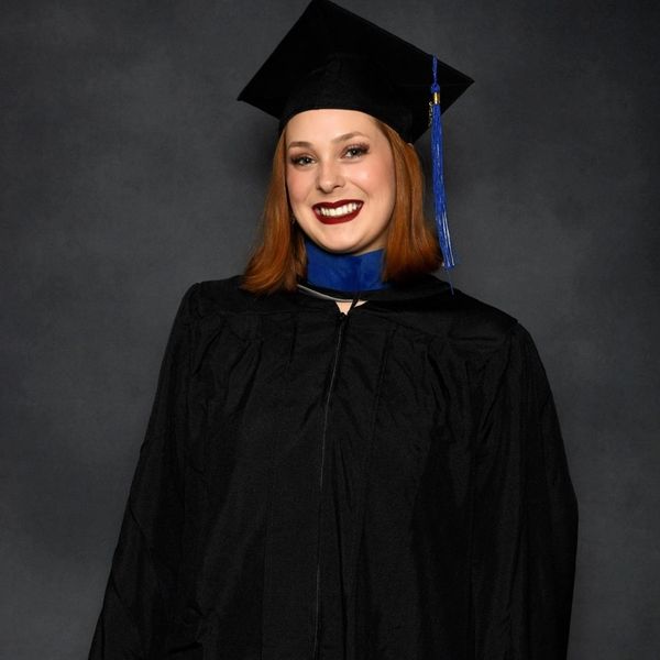 Smiling graduate in black cap and gown with blue tassel and collar.
