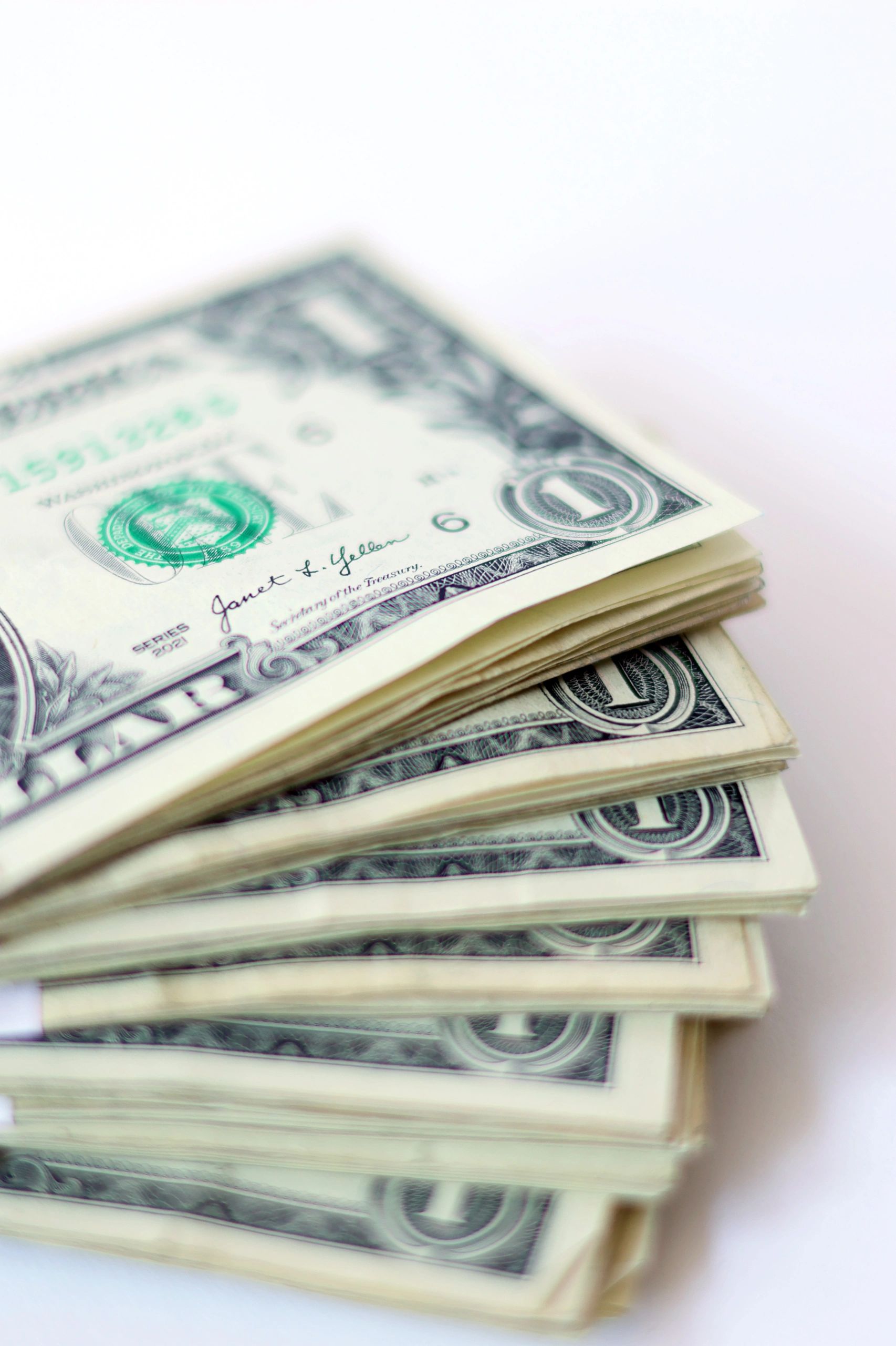 Stack of one-dollar bills fanned out on a white surface.