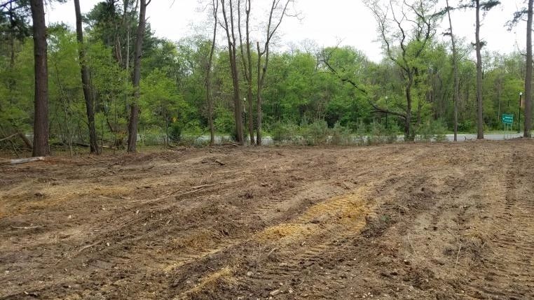 Cleared and tilled soil area near a forest and road.