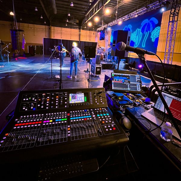 Sound mixing console in a live music venue with band performing on stage.