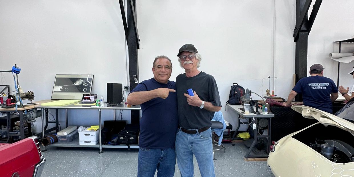Two men posing together in a garage or workshop.