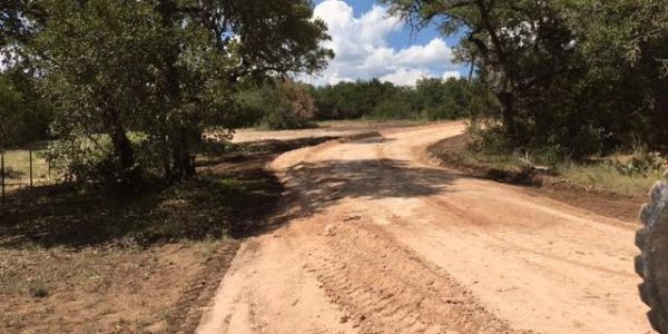 Winding dirt road surrounded by trees under a blue sky.