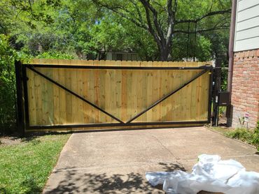 Wooden driveway gate with metal frame and trees in the background.