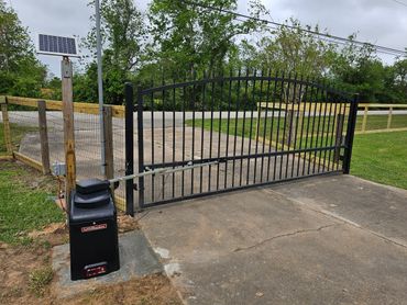 Black metal gate with a solar panel and gate opener on a driveway.