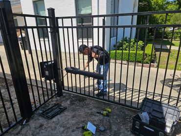 Man installing or repairing a black iron gate with tools around.