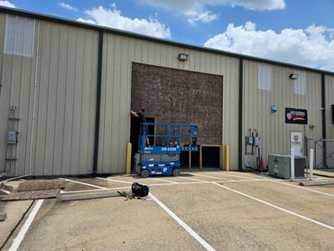 Man working on a building exterior using a blue lift under a partly cloudy sky.