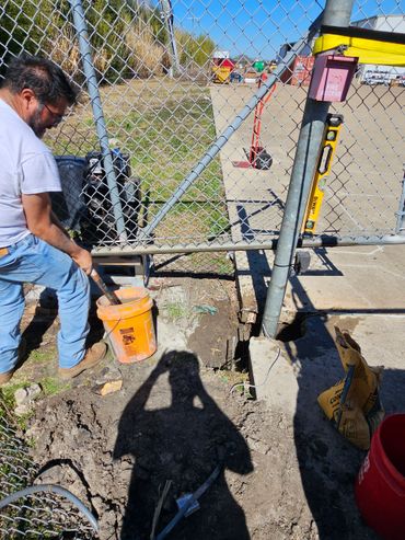 Man working on a chain-link fence with tools and cement.