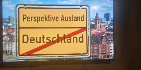Sign indicating 'Perspective Abroad' and crossing out 'Germany' with cityscape background.