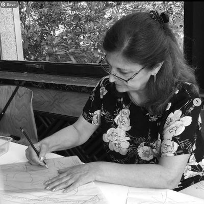Woman drawing at a table in a floral shirt with glasses.