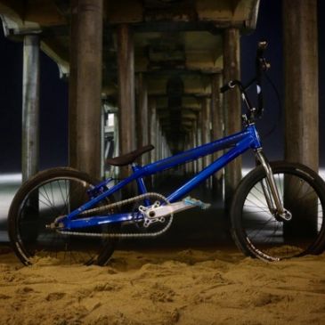 Blue BMX bike on sandy beach at night under pier.