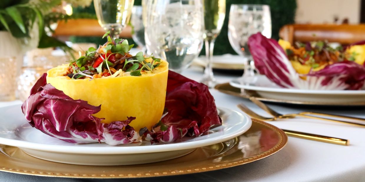 Plated stuffed yellow bell pepper with quinoa filling on white table with gold accents
