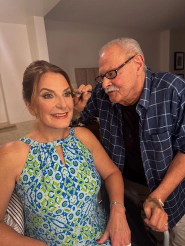 Man applying eye makeup on a smiling woman in a patterned dress.
