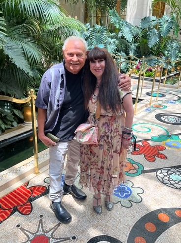 A smiling couple posing indoors with lush plants and colorful mosaic floor.