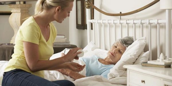 In Home Caregiver offering medication dispensing to client in bed.