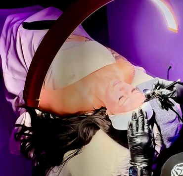 Woman receiving a detailed facial treatment under bright lamp.