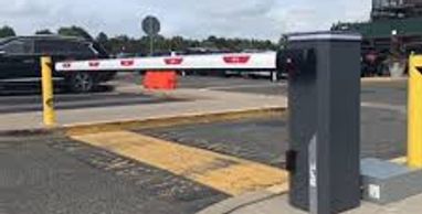 Automated gate barrier at a parking lot entrance under a cloudy sky.