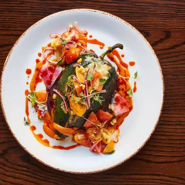 Stuffed poblano pepper with colorful vegetables and sauce on a white plate.