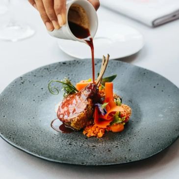 Gourmet lamb chops with sauce and vegetable garnishes on a stylish plate.