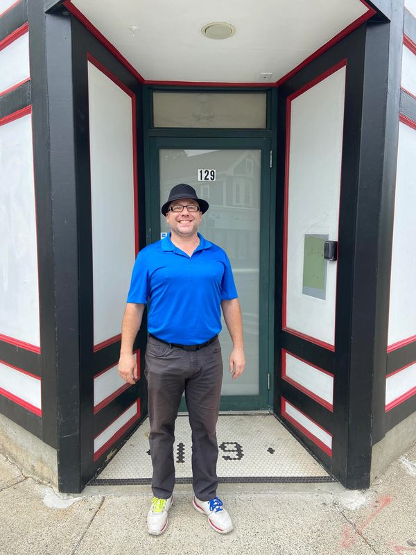 Man in blue shirt and black trillby and pants in front of 129 Pearl St Somerville MA