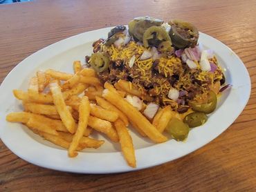 Plate of chili cheese fries topped with jalapeños and onions.