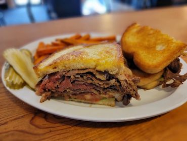A roast beef sandwich with toasted bread, pickles, and fries on a white plate.