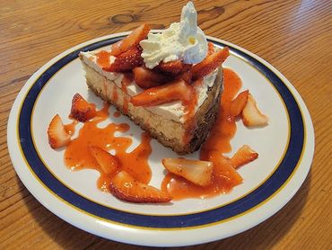 Slice of cheesecake topped with whipped cream and fresh strawberries on a white plate.