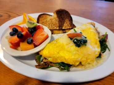 A breakfast plate with an omelette, toast, and a bowl of fresh fruit.