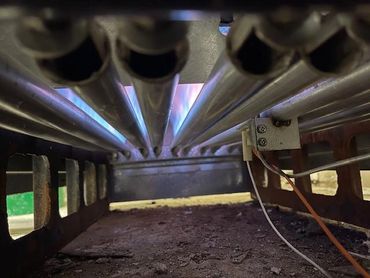 Close-up view inside a gas furnace burner with visible blue flames.