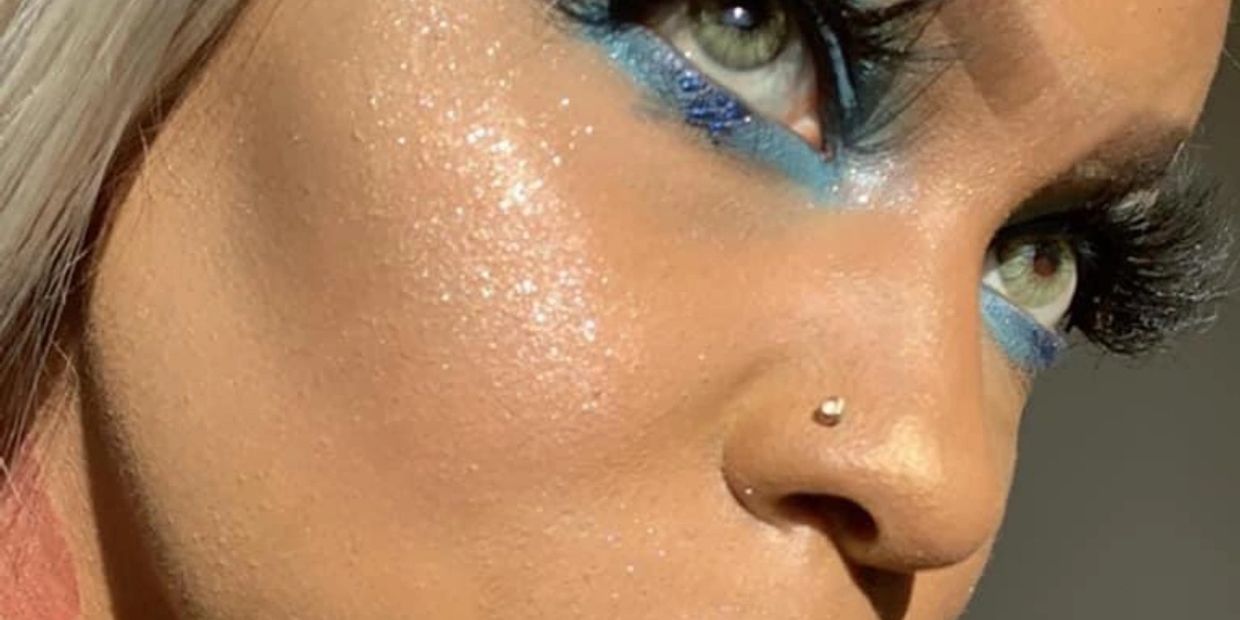 Close-up of a face with blue eye makeup and a nose piercing.