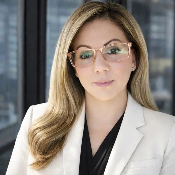 Professional woman with blonde hair and glasses wearing a white blazer.