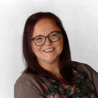 Smiling woman with glasses and reddish-brown hair.