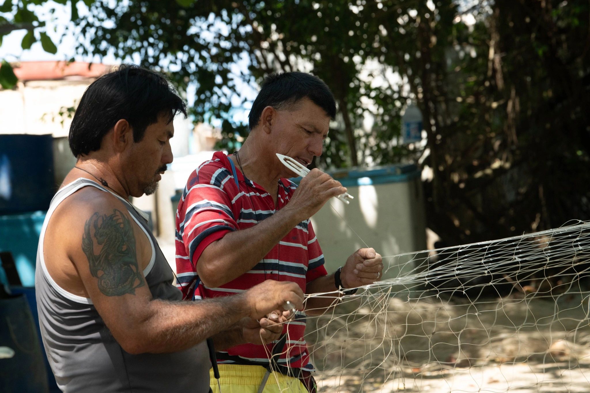 Dos hombres reparan una red de pesca al aire libre.