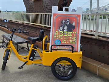 Yellow tricycle with a sign advertising Abbey Road on the River event.