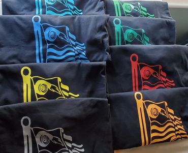 Folded black shirts with colorful flag designs in blue, green, yellow, red, orange, and white.