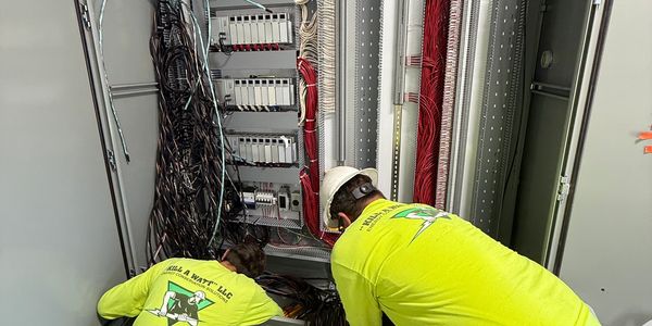Two electricians working on wiring inside a control panel.