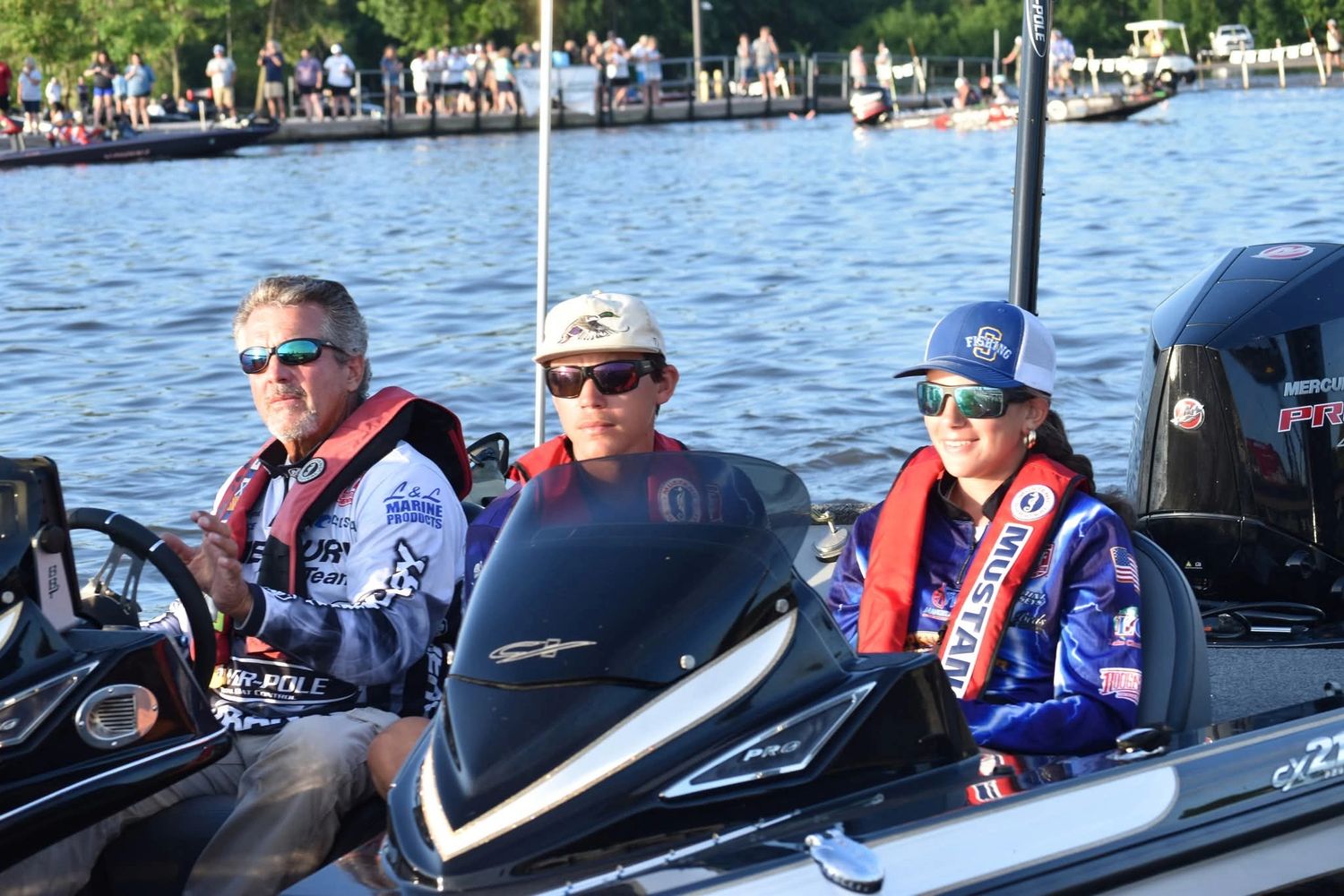 Three people wearing life jackets and sunglasses on a boat on the water.