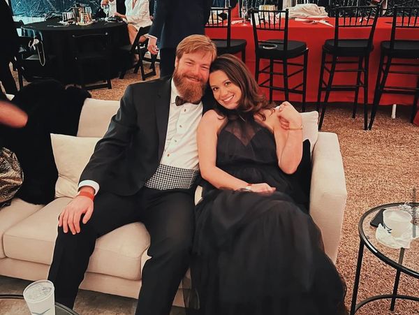 A smiling couple in formal attire sitting on a white couch at an event.